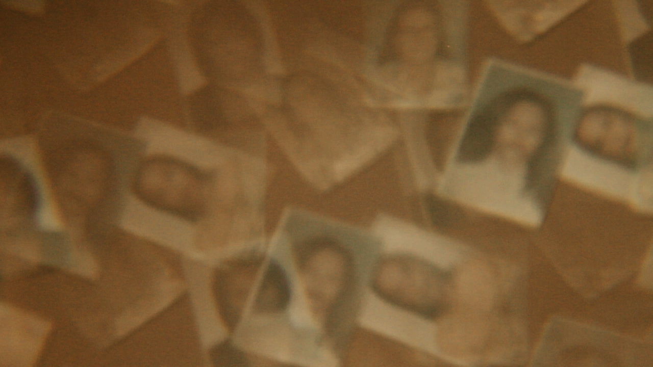Pessoa segura uma fotografia antiga sobre um caixote com fitas de vídeo e papéis, durante pesquisa sobre filmes de família no Loteamento Nuporanga, em Maceió, maio de 2025.